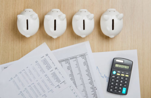 Four piggy banks sit on a desk along with financial documents and a calculator.