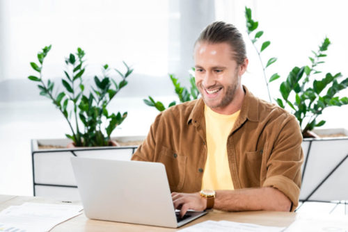 A man smiles as he types away on his laptop.