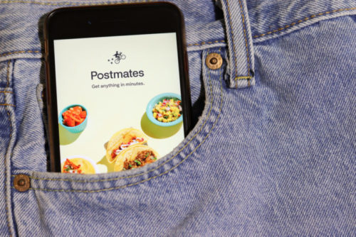 A closeup of a smartphone in a pocket displaying the Postmates app.