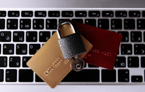 A laptop sits under some credit cards, which sit under a lock and key.