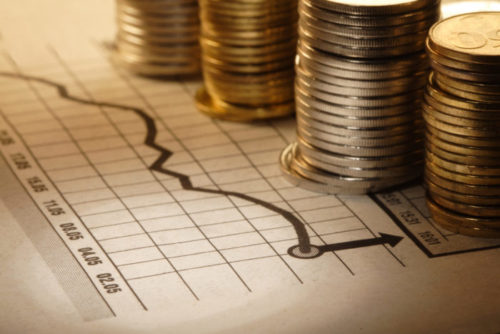 Foreign currency coins sitting in stacks on top of a stock market chart.