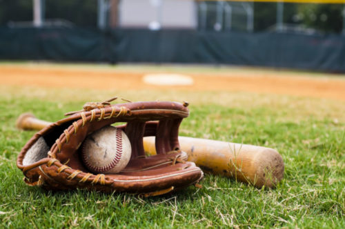 An old glove and bat lie on a baseball field.