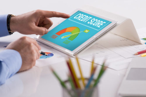 A man pointing at a tablet with a screen that displays a credit score gauge, while analyzing a financial chart on his desk.