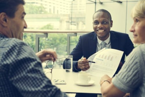 A banker holding up financial documents and pointing at them with a pen while speaking to his clients.