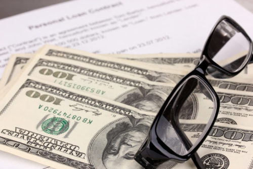 Eyeglasses and cash sit on top of a personal loan contract.
