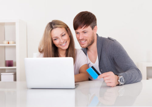 A smiling couple using their laptop, while the male holds a credit card.