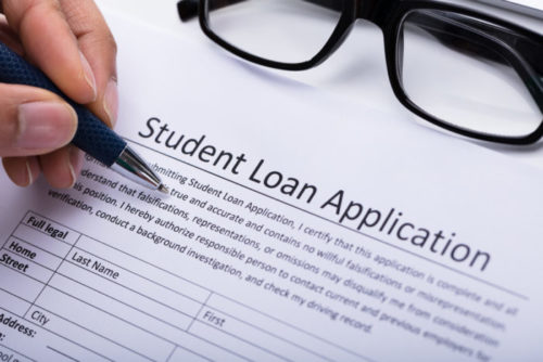 A close up of a person's hand filling out a student loan application.