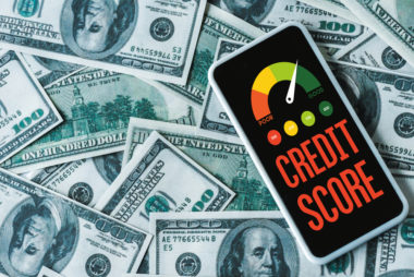 A smartphone displaying a credit score gauge lies on top of $100 bills.