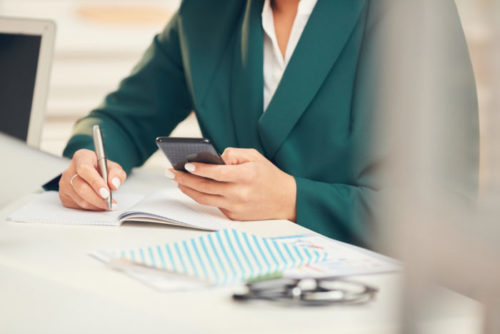 A financial advisor writing in a notebook, holding her smartphone.