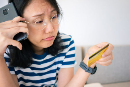 A sad looking woman speaking on the phone while holding her credit card.