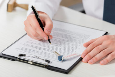 A man signing a document with house keys sitting on top of it.