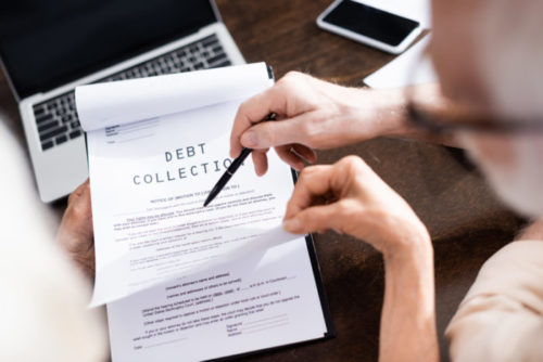 A person pointing to a document labeled "debt collection" with a pen.