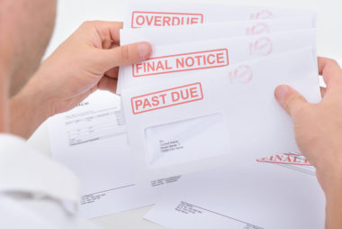 A man holding several envelopes stamped "overdue," "final notice," and "past due."
