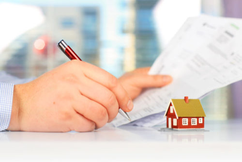 A man signing a document with a tiny model house on his desk.