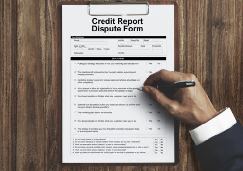 A businessman's hand holding a pen over a credit report dispute form.