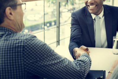 A smiling banker greets his client with a handshake.