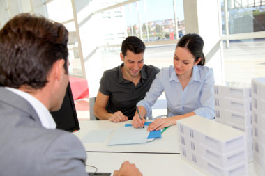 An insurance agent watches a smiling couple sign a document.