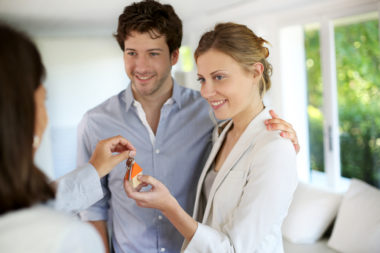 A mortgage agent hands a smiling couple the keys to their new house.