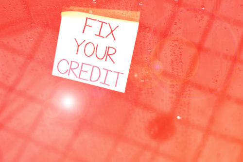 A post it note that reads "fix your credit" is stuck on a pink wall.