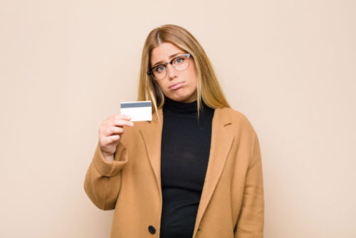 A sad looking woman holding up her credit card.