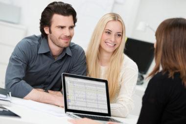 An insurance agent sharing financial figures from her computer screen to a smiling couple.