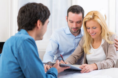 A bank representative handing over a document for a couple to sign.