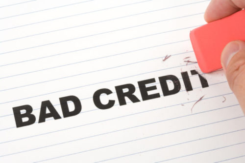 A closeup of someone's hand holding a pink eraser, and erasing the words "bad credit."