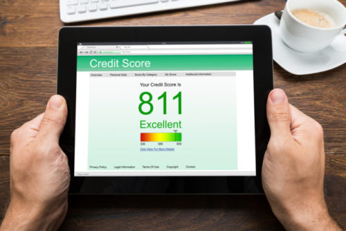 A person's hands hold a tablet which displays a credit score screen. The credit score is 811 with the work "excellent" below the score.