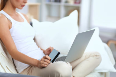 A woman shopping online with her computer on her lap and a credit card in her hand.