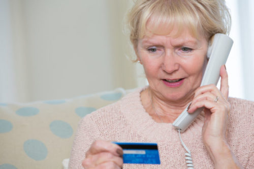 An elderly woman reading her credit card information to someone over the phone.