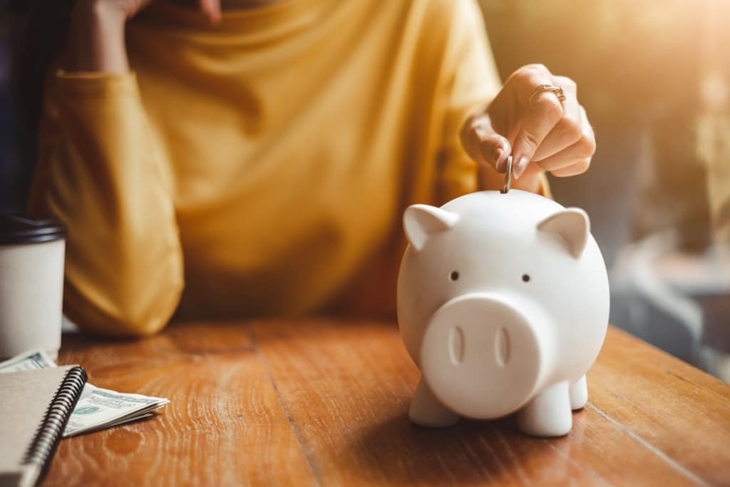 A woman's hand putting a coin into a white piggy bank on a table