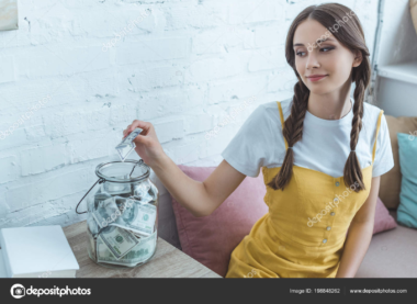 A woman putting cash into a glass savings jar.