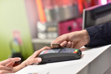 A store clerk holds a payment terminal for a person to swipe their credit card through.