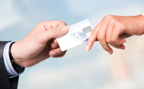 A person in business attire hands a store clerk a credit card.