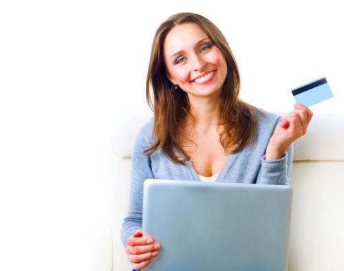 A smiling woman shops online while holding a credit card.