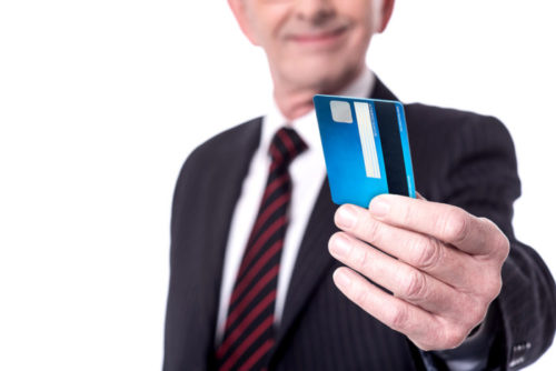 A person in business attire extends a credit card toward the camera.