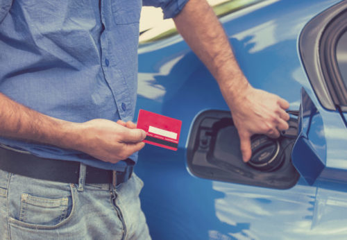 A man holding a credit card while opening the fuel tank of his car.