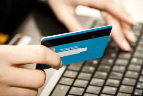 A closeup of a person typing on their laptop while holding their credit card.