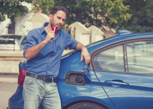 A man opening the fuel tank of his car while holding a credit card.