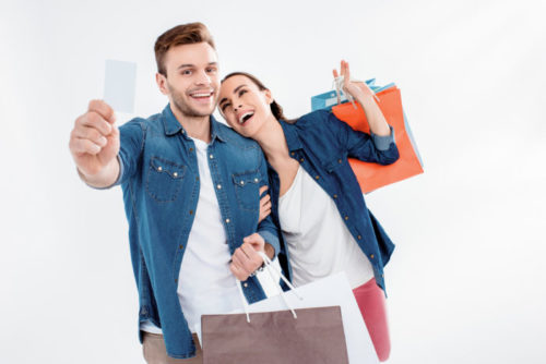 The man of a smiling couple out shopping holds up a credit card.