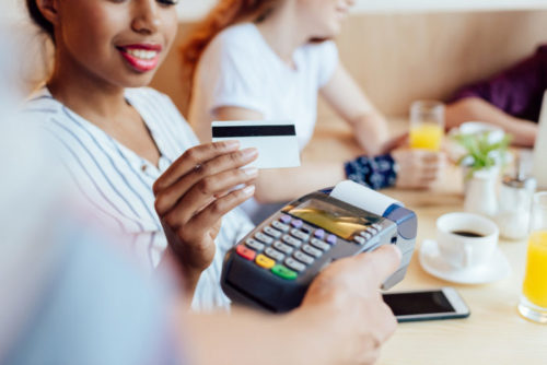 A barista holds a payment terminal for a person to swipe their credit card into to pay for their coffee.