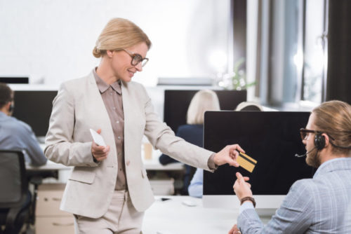 A person wearing business attire handing a colleague a credit card in the office.