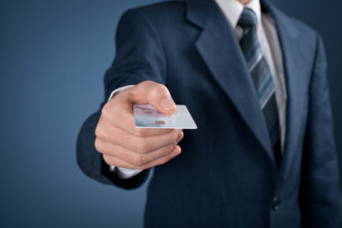 A businessman extends a credit card toward the camera.