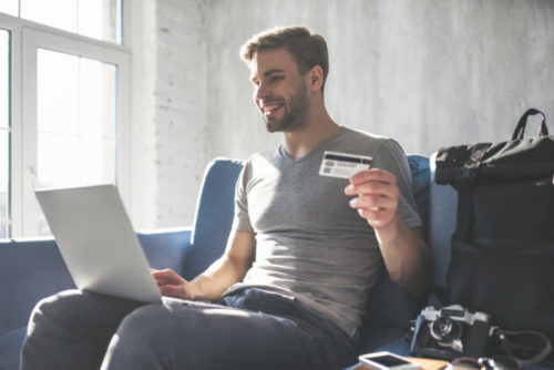 A man using his laptop in an airport holding up his credit card.