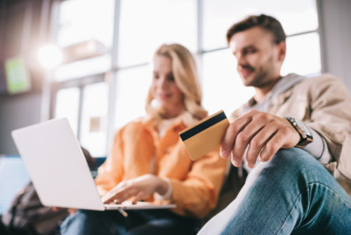 A couple in an airport looking at their laptop while the man holds a credit card.