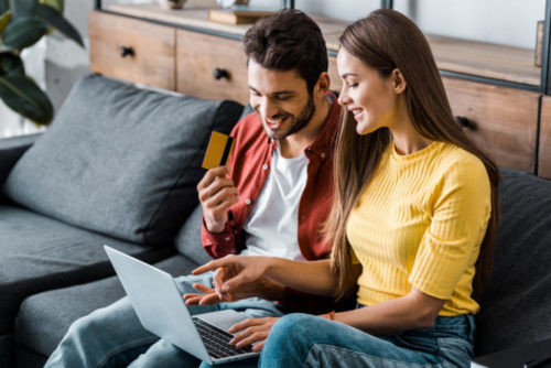 The man of a smiling couple holds a credit card while they shop online.