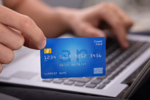 A closeup of a man holding a credit card above his laptop.