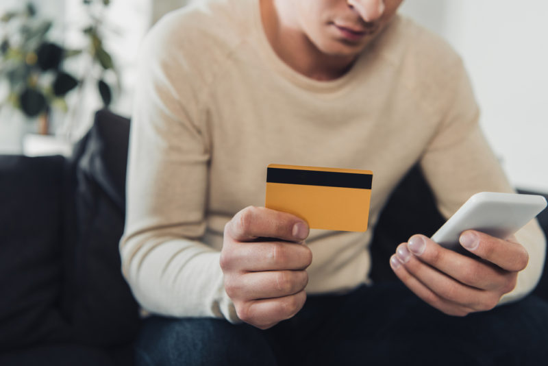 A man making a purchase on his phone holds up his credit card.