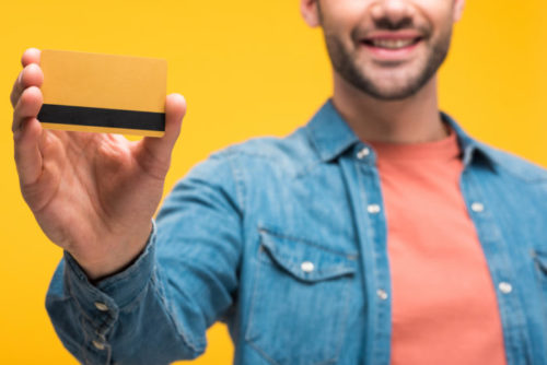 A smiling man holding up a gold credit card.