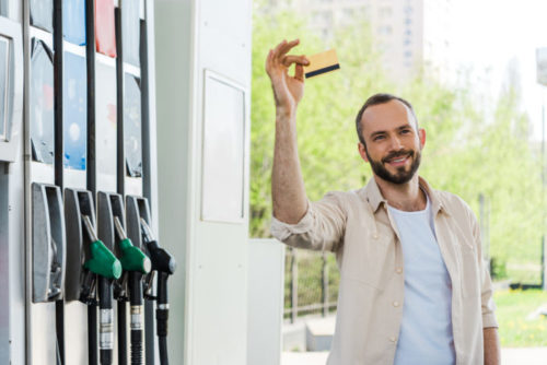 A man holding up a credit card at a fuel pump.